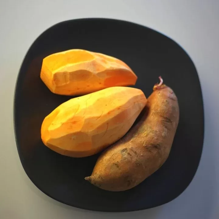 Batata doce com casca e descascada, em cima de um prato preto e fundo cinzento